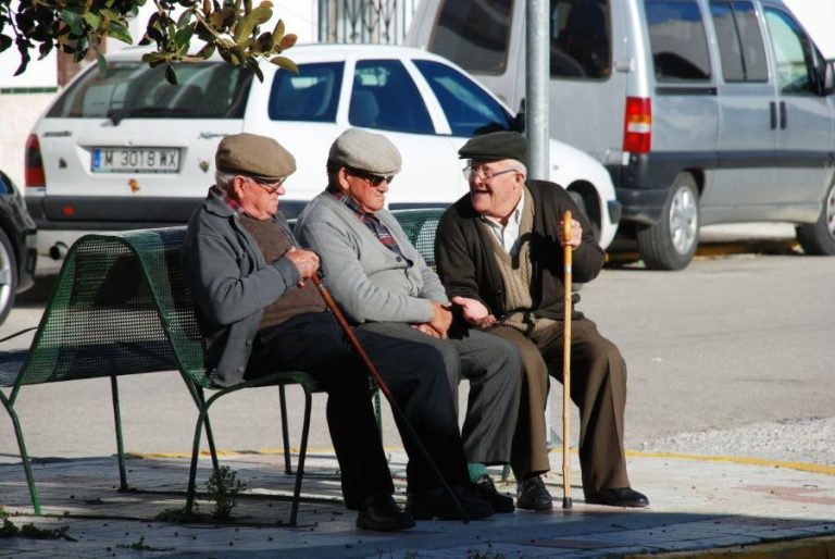 Tres hombres mayores conversan sentados en un banco | Foto de 123RF/arenaphotouk
